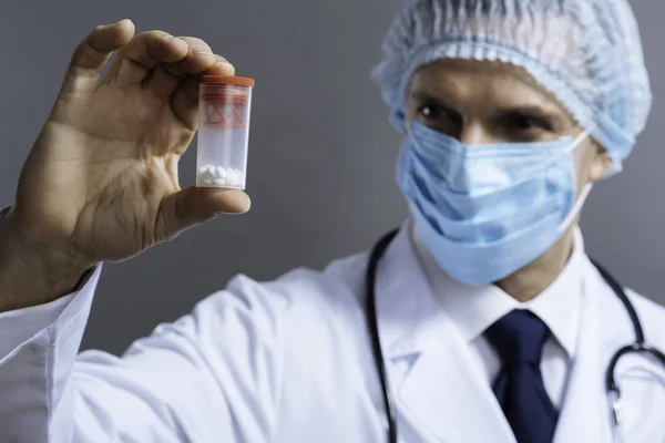 Médico sério na máscara facial segurando caixa com pílulas — Fotografia de Stock