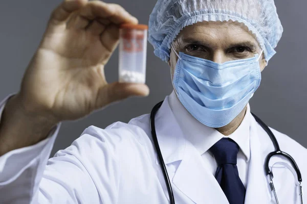 Bonito médico na máscara facial posando com pílulas caixa — Fotografia de Stock