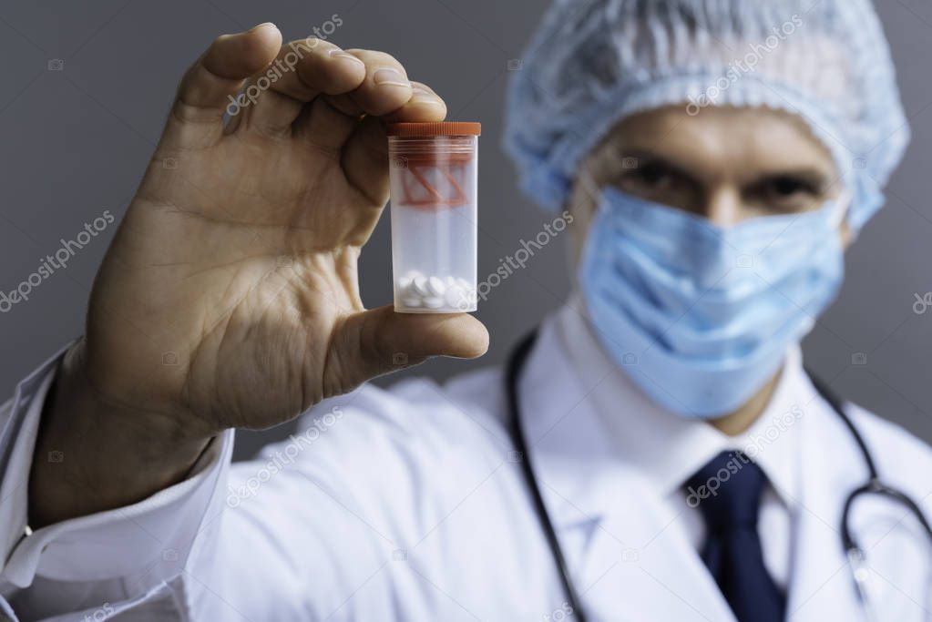 Confident doctor in face mask holding pills box