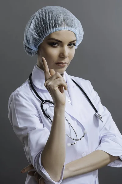 Vrouwelijke arts gebaren met haar vinger op grijze achtergrond — Stockfoto