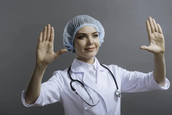 Médico feminino colocando as mãos para cima em fundo cinza . — Fotografia de Stock