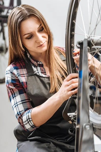 Mujer positiva reparando la bicicleta de ruedas en el taller de reparación — Foto de Stock
