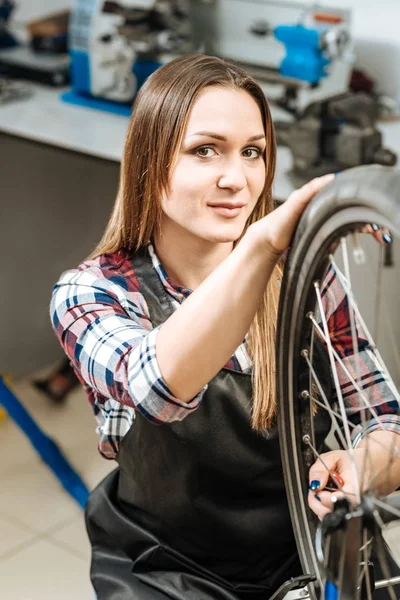 Encantadora mujer reparando la bicicleta de ruedas en el taller de reparación — Foto de Stock
