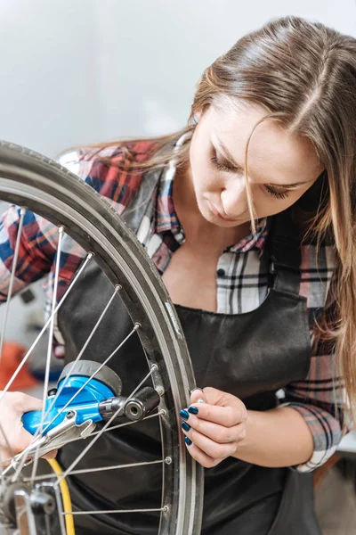 Joven atenta artesana fijando la rueda de la bicicleta — Foto de Stock