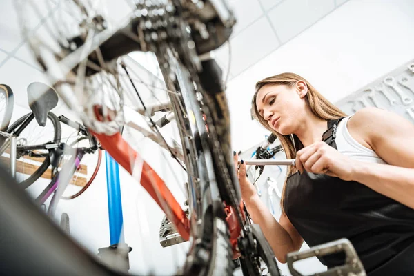 Aufmerksame Arbeiterin repariert Fahrrad in der Garage — Stockfoto