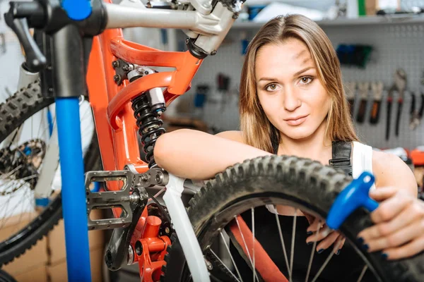 Attractive female technician repairing the bicycle in the garage — Stock Photo, Image