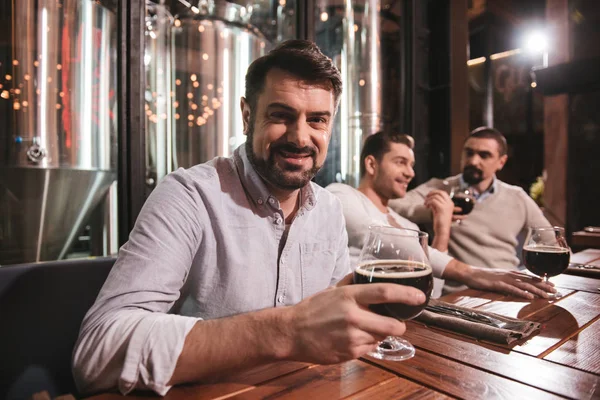 Alegre buen hombre poniendo un vaso con cerveza en la mesa —  Fotos de Stock