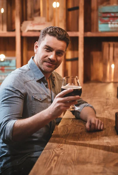 Hombre guapo positivo sosteniendo un vaso con bebida alcohólica — Foto de Stock