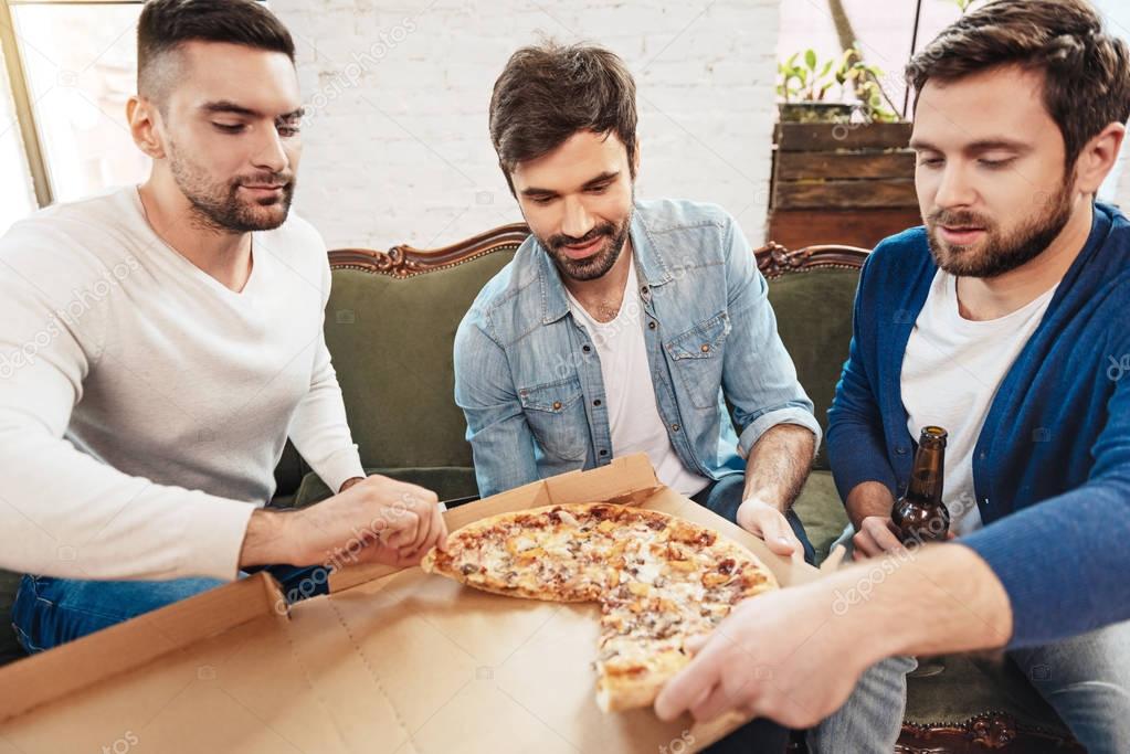 Attractive young men taking slices of pizza