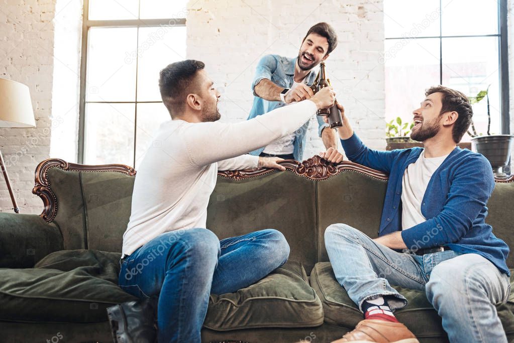 Cheerful delighted men raising bottles with beer