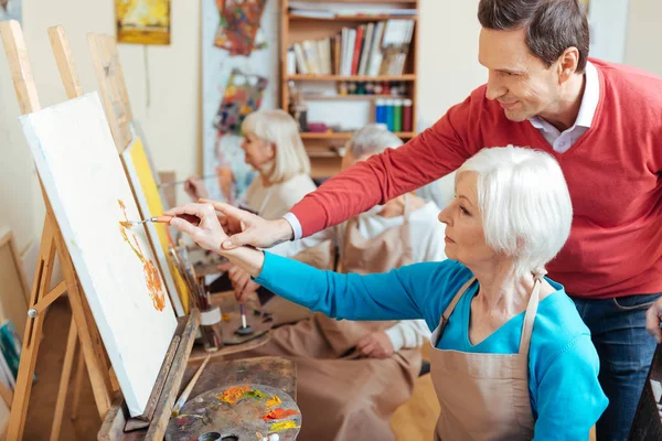 Восхитительный художник, помогающий пожилой женщине в студии живописи — стоковое фото