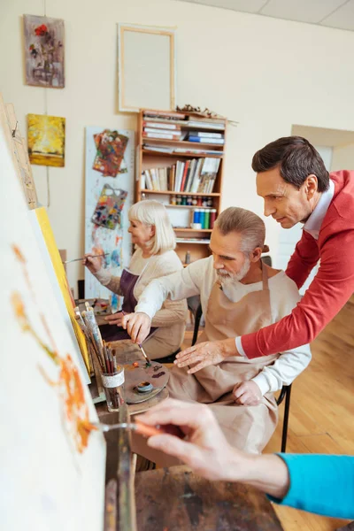 Radosny artysta pomaga starszego mężczyzny w studio malarstwa — Zdjęcie stockowe