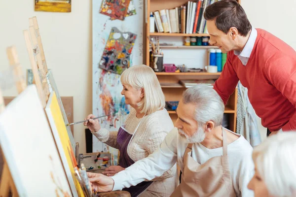 Handsome artist controlling his colleagues in painting class — Stock Photo, Image