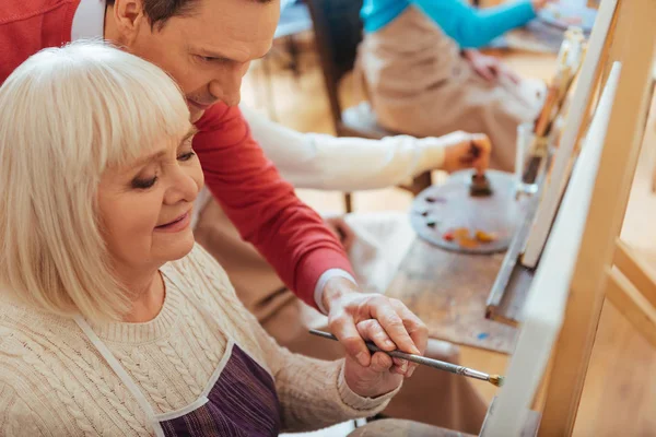Concentrated man helping elderly woman in painting studio — Stock Photo, Image
