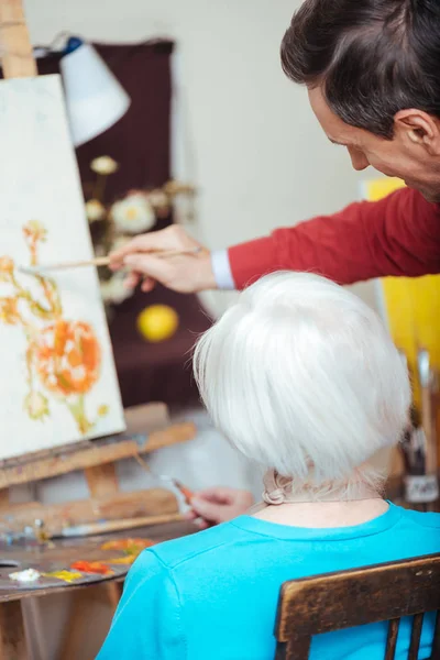 Профессиональный художник преподает пожилую женщину в школе живописи — стоковое фото