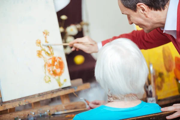 Talentoso artista enseñando a anciana en escuela de pintura —  Fotos de Stock