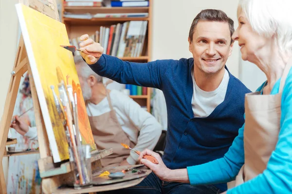 Радостный художник помогает пожилой женщине в живописи — стоковое фото