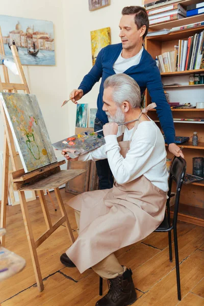 Ambitious artist helping elderly man in painting — Stock Photo, Image