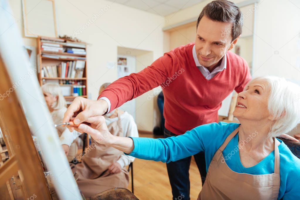 Smiling artist helping elderly woman in painting studio