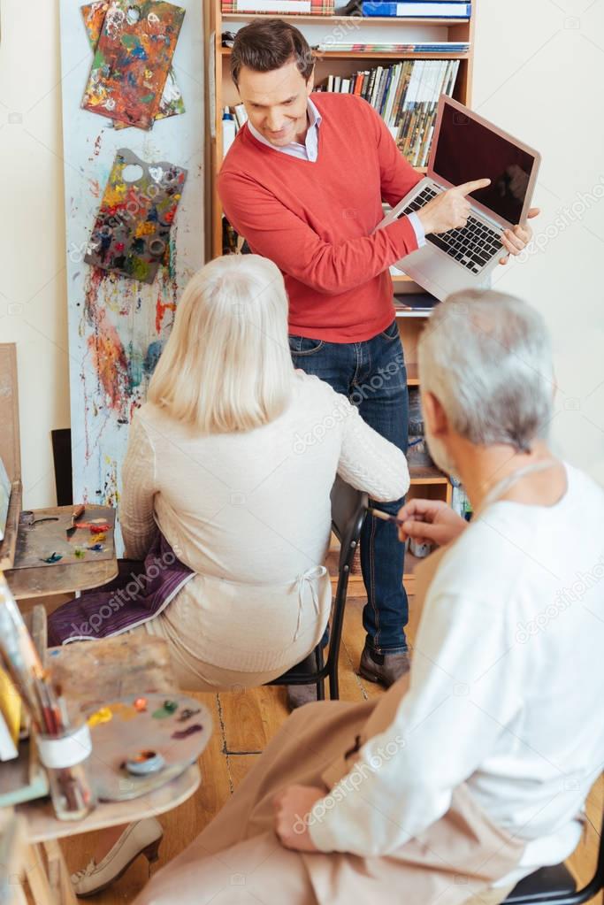 Delighted man showing laptop to colleagues in painting studio