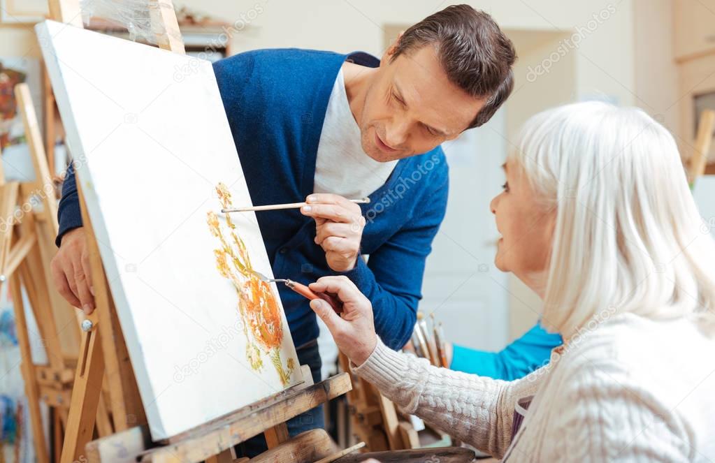 Serious artist helping elderly woman in painting school
