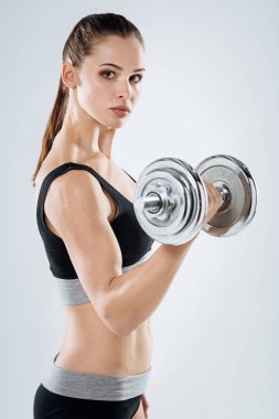 Gri bir arka plan üzerinde dumbbell tutarak kendine güvenen kız