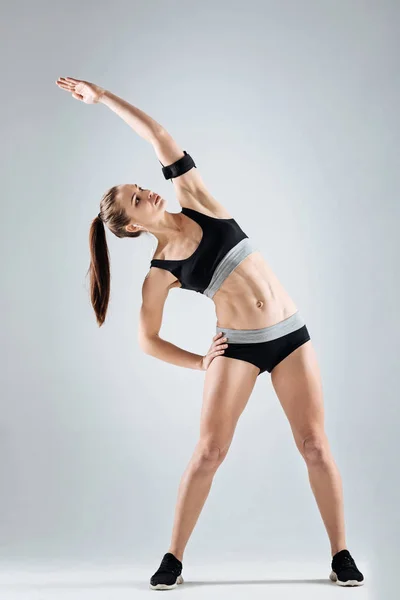 Chica motivada haciendo ejercicios sobre un fondo gris — Foto de Stock