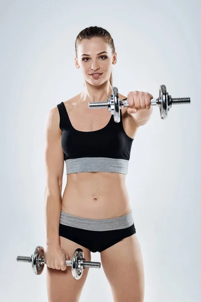 Chica encantada haciendo ejercicio con pesas sobre un fondo gris — Foto de Stock