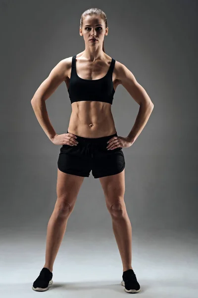 运动女孩展示她的肌肉在灰色的背景上 — 图库照片