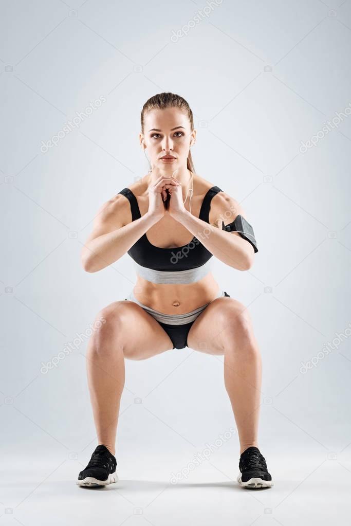Concentrated girl doing knee bands on a grey background