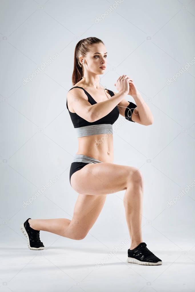 Concentrated girl doing lunges on a grey background