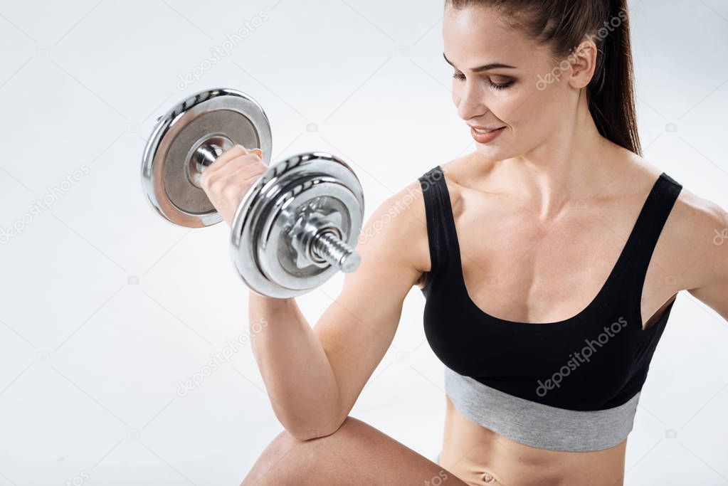 Concentrated girl posing with dumbbells on a grey background