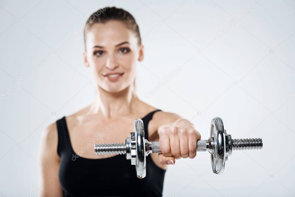 Overjoyed girl exercising with dumbbells on a grey background