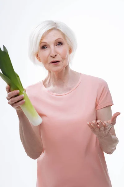 Удивлённая пожилая женщина держит лук-порей в правой руке — стоковое фото