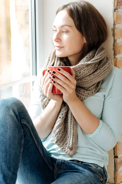 Delighted charming girl drinking tea on the windowsill — Stock Photo, Image