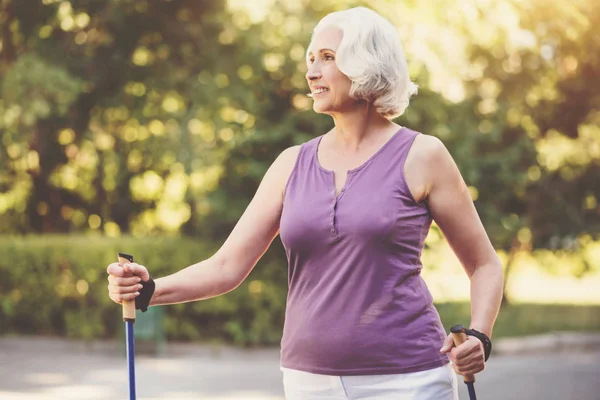 Vrolijke grijze donkerharige vrouw houden walking stokken — Stockfoto