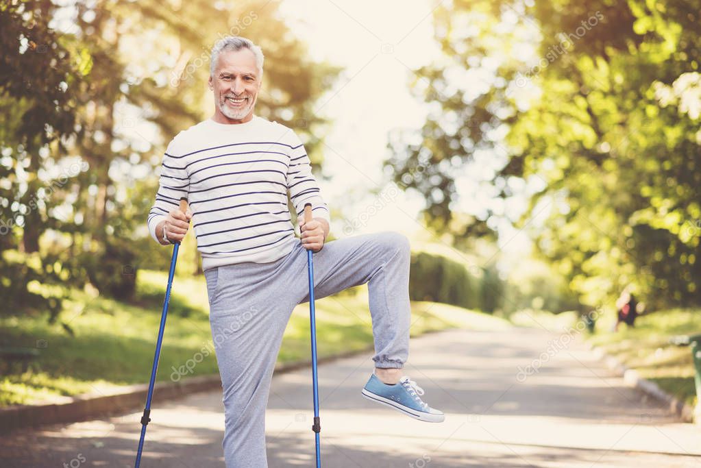 Joyful aged man practicing Nordic walking