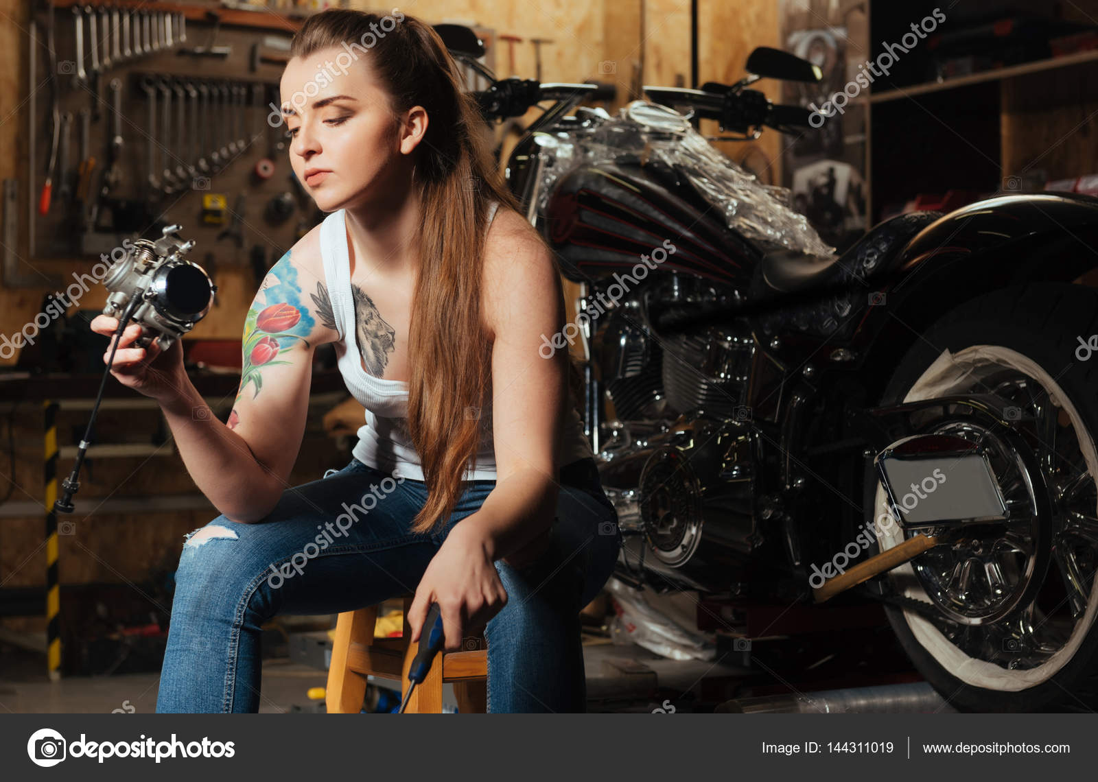Serious female biker keeping screwdriver in left hand Stock Photo by