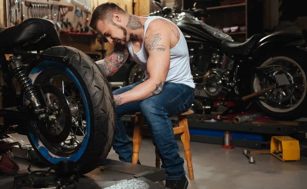 Positive delighted brutal biker fixing wheel — Stock Photo, Image