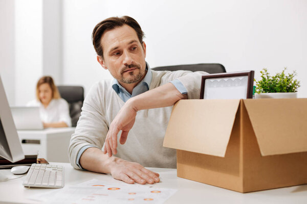 Thoughtful manager holding the box and sitting in the office