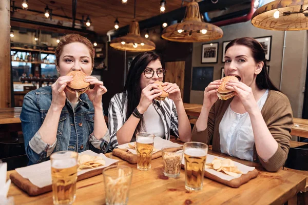 Empresa de meninas encantadas degustação de hambúrgueres — Fotografia de Stock