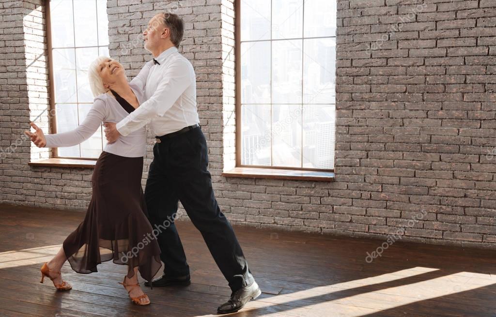 Delighted senior couple enjoying tango at the ballroom