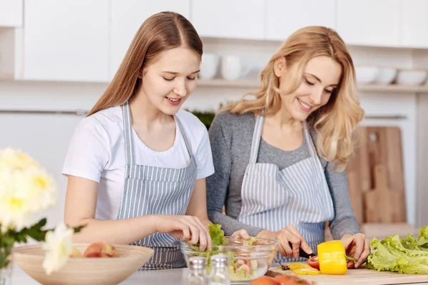 Улыбающаяся девочка-подросток и ее мать готовят на кухне — стоковое фото