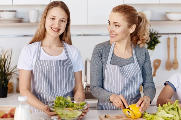 Alegre chica sonriente cocina ensalada de verduras con su madre — Foto de Stock