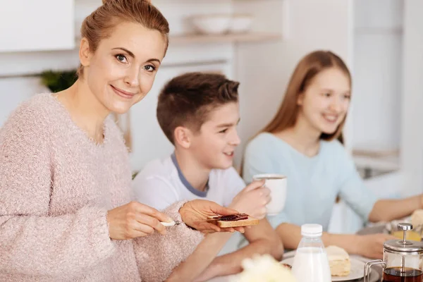 Mãe carinhosa alegre tomando café da manhã com seus filhos — Fotografia de Stock