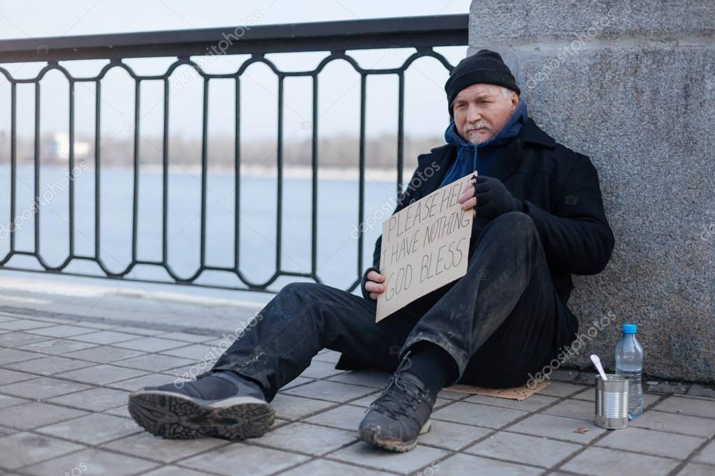 Homeless gray-haired man sitting on the tile