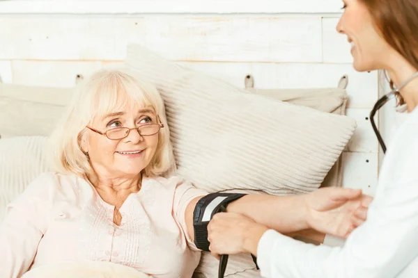 Behendig verzorger gepensioneerden bloeddruk thuis meten — Stockfoto