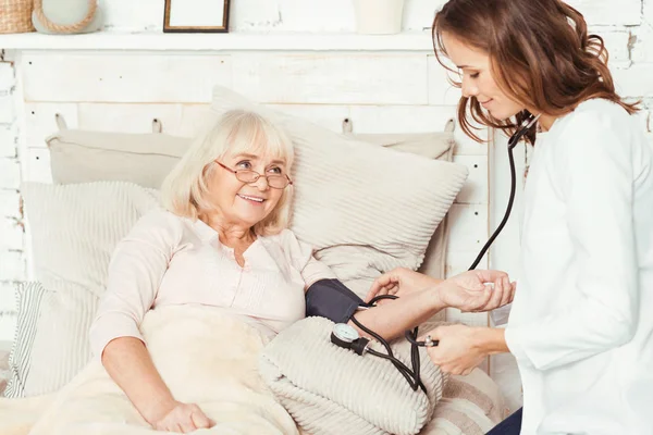 Careful caregiver measuring patients blood pressure at home — Stock Photo, Image