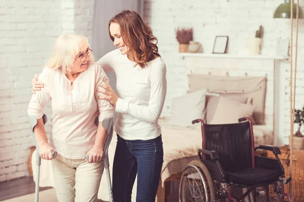 Vrolijke jonge vrouw helpen uitgeschakeld oude dame thuis — Stockfoto