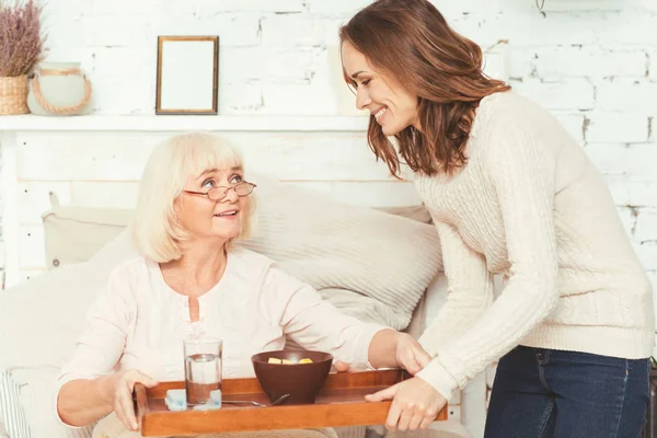 Positive young granddaughter taking care of pensioner at home — Stock Photo, Image